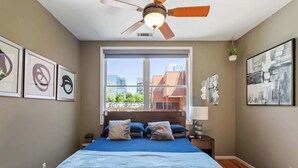 A bedroom with a large window, a ceiling fan, and artwork on the walls. - Warehouse District Modern Condo w/ Private Garage (Raleigh)