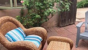 Mobilier en osier agrémenté de coussins, une clôture en bois et un arbuste en fleurs dans un espace patio extérieur.