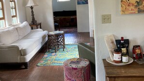 Un salon avec un canapé blanc, un tapis à motifs, une table basse en bois et un petit tabouret. Il y a un tableau au mur et une fenêtre qui laisse entrer la lumière naturelle.