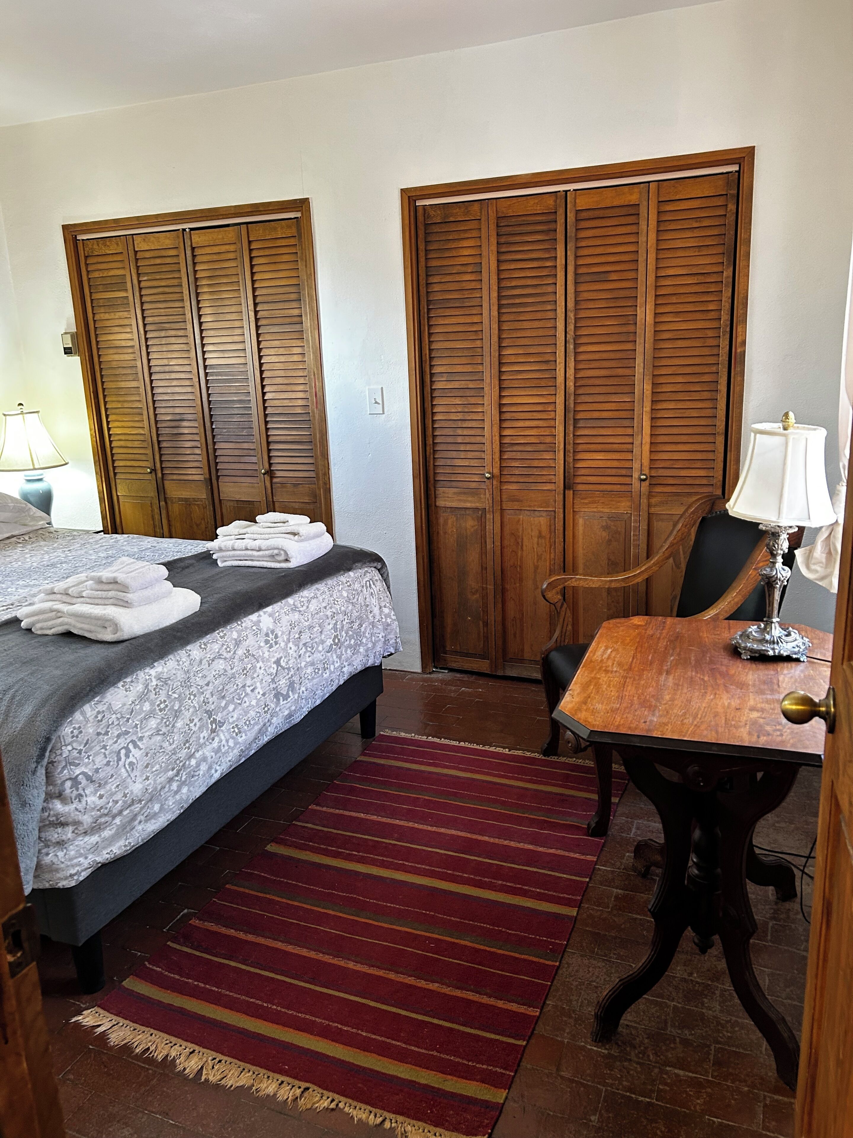 A hotel room with a bed, a desk, a chair, and two wooden wardrobes.