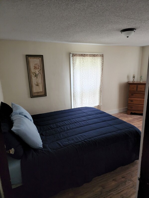 A bedroom with a bed, a dresser, a framed picture on the wall, and a window with curtains.