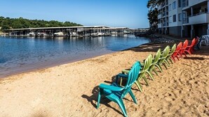 Una playa con una fila de sillas de colores, un edificio con balcones y un puerto deportivo al fondo.