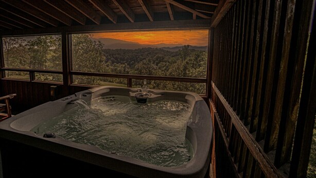 Ein Whirlpool mit Blick auf einen Sonnenuntergang über einer bewaldeten Landschaft.