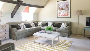 A living room with a sectional sofa, a white ottoman, a patterned rug, a television, and a framed picture on the wall.