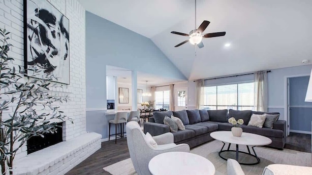 A modern living room with a white brick fireplace, grey sofas, and a ceiling fan. - Hot Tub | Sauna | Pets Allowed | Sleeps 10 (Leander)