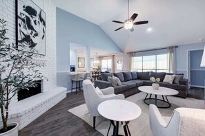 Una sala de estar moderna con chimenea de ladrillo blanco, sofás grises y un ventilador de techo.