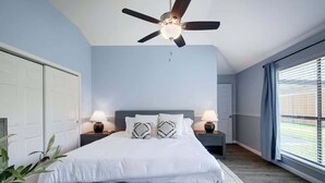 A bedroom with a bed, nightstands, a ceiling fan, and a window with blinds. - Hot Tub | Sauna | Pets Allowed | Sleeps 10 (Leander)
