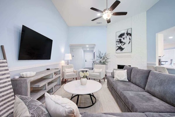 Una sala de estar moderna con un sofá gris, una mesa de centro blanca y un televisor de pantalla plana montado en la pared.