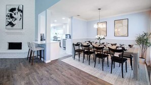A modern dining area with a white brick wall, a fireplace, and a dining table set for six. - Hot Tub | Sauna | Pets Allowed | Sleeps 10 (Leander)
