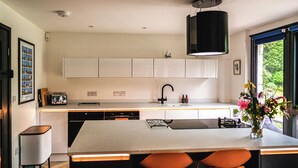 A modern kitchen with white cabinets, a black faucet, and a large island with bar stools. - 5 bedroom accommodation in Chilcompton (Chilcompton)