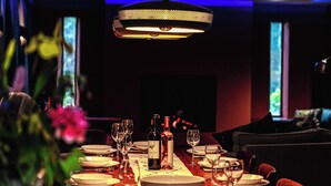 A dining table set for a meal with plates, glasses, and a bottle of wine, in a dimly lit room with a modern chandelier. - 5 bedroom accommodation in Chilcompton (Chilcompton)
