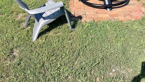 Un patio con una mesa redonda y dos sillas, rodeado de césped y árboles.