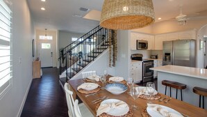 A dining area with a wooden table set for four, a kitchen with modern appliances, and a staircase leading to another level.