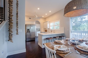 A modern kitchen with white cabinetry, a central island, and a dining area set for six with a large window providing natural light. - Beach House ! Sunset Decks ! Walk to Beach & John's Pass Boardwalk (Treasure Island)