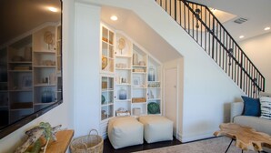 A spacious living area with a built-in bookshelf, a staircase with a black railing, and a light-colored sofa.