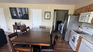 Zona pranzo con tavolo e sedie in legno, cucina con elettrodomestici e una porta che dà su un'altra stanza.