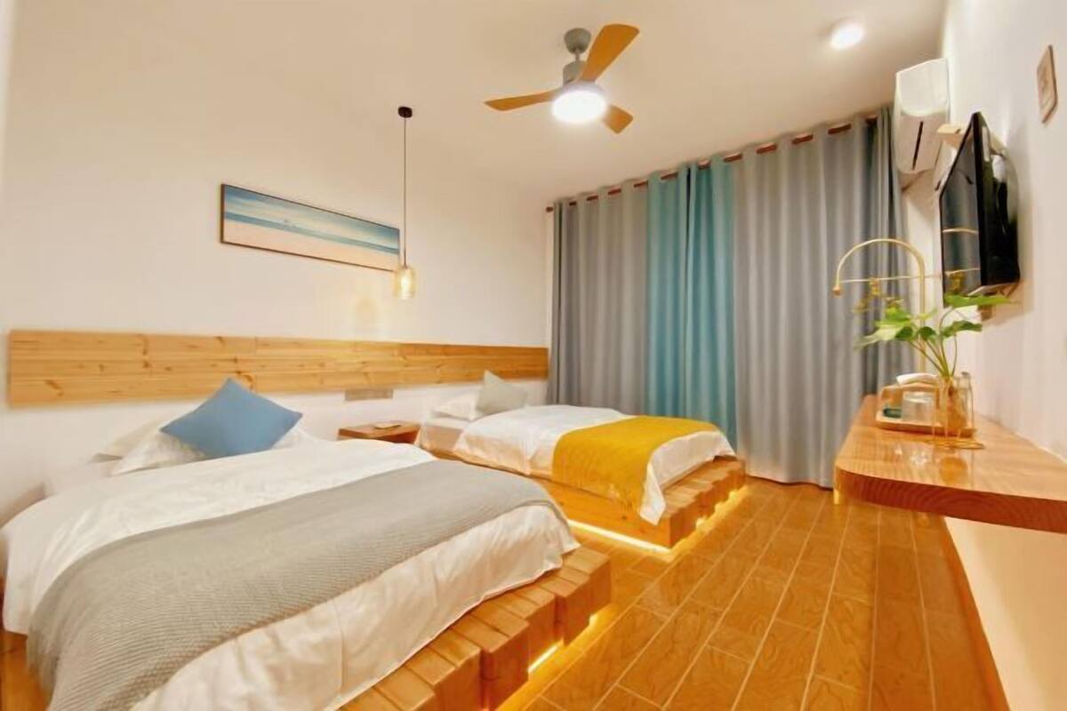 A hotel room with two beds, a ceiling fan, a mounted TV, and a bedside table with a plant.