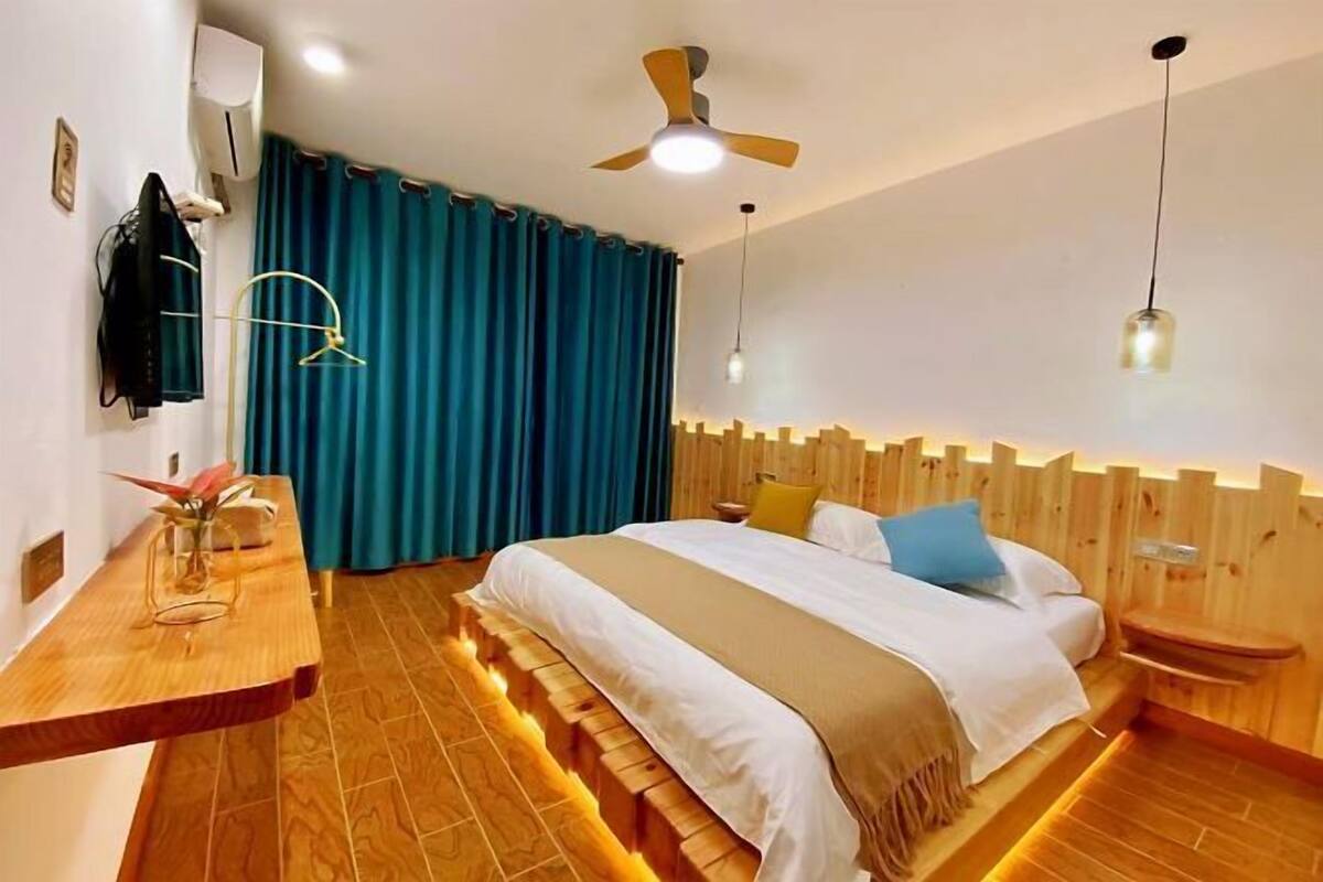 A modern hotel room with a wooden bed, a wooden desk, a ceiling fan, and a large window with curtains.