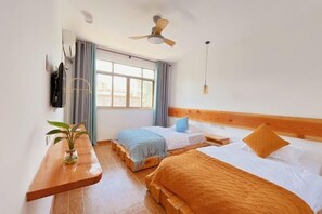 A hotel room with two beds, a wooden bench, a plant, a ceiling fan, and a window with curtains.