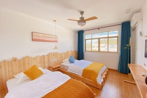 Quarto com duas camas, um ventilador de teto, janela com cortinas e uma escrivaninha.
