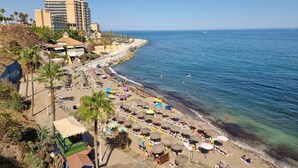 A beach with rows of sun loungers and umbrellas, a hotel in the background, and the ocean.