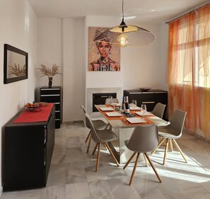 Un espace repas moderne avec une longue table dressée pour six personnes, un buffet noir, un chemin de table rouge et un tableau accroché au-dessus de la table.