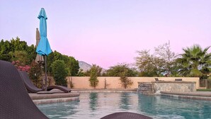 A pool area with lounge chairs, a blue umbrella, and a stone water feature. - Private Large Modern Villa with Pool/Spa/Slide (Cathedral City)