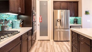 A modern kitchen with dark wood cabinets, stainless steel appliances, and a tiled backsplash. - Private Large Modern Villa with Pool/Spa/Slide (Cathedral City)