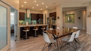 A modern kitchen with a central island, bar stools, and a dining table with chairs. - Private Large Modern Villa with Pool/Spa/Slide (Cathedral City)