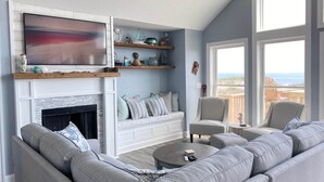 Ein Wohnzimmer mit Kamin, großem Fernseher und Blick auf den Strand.