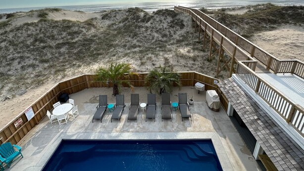 Ein Poolbereich direkt am Strand mit Liegestühlen, einer Holzterrasse und Blick aufs Meer.