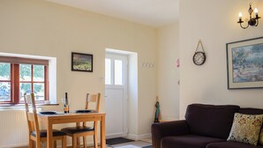 A living room with a wooden dining table, a brown sofa, a coffee table, and a painting on the wall. - A charming countryside cottage break. (Cwmdu, Near Llandeilo)