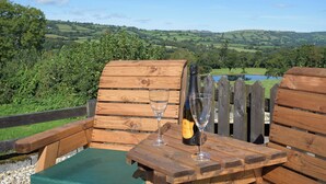 A wooden table with a bottle of wine and a glass, set against a scenic view of rolling hills and a lake. - A charming countryside cottage break. (Cwmdu, Near Llandeilo)