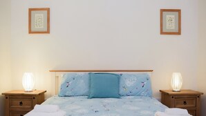 A neatly made bed with floral bedding, two bedside lamps, and a framed picture on the wall. - A charming countryside cottage break. (Cwmdu, Near Llandeilo)