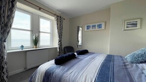 A bedroom with a large bed, a view of the sea through a window, and a chair. - 2 bedroom accommodation in Portmahomack (Portmahomack)