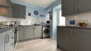 A modern kitchen with grey cabinets, a washing machine, and a microwave. - 2 bedroom accommodation in Portmahomack (Portmahomack)