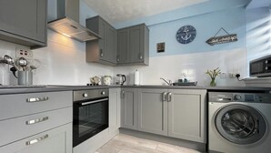 A modern kitchen with grey cabinets, a built-in oven, a washing machine, and a clock on the wall. - 2 bedroom accommodation in Portmahomack (Portmahomack)