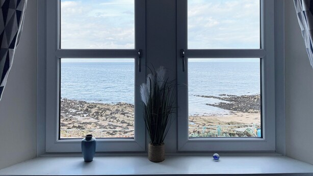 A room with a bay window overlooking a rocky beach and the sea. - 2 bedroom accommodation in Portmahomack (Portmahomack)
