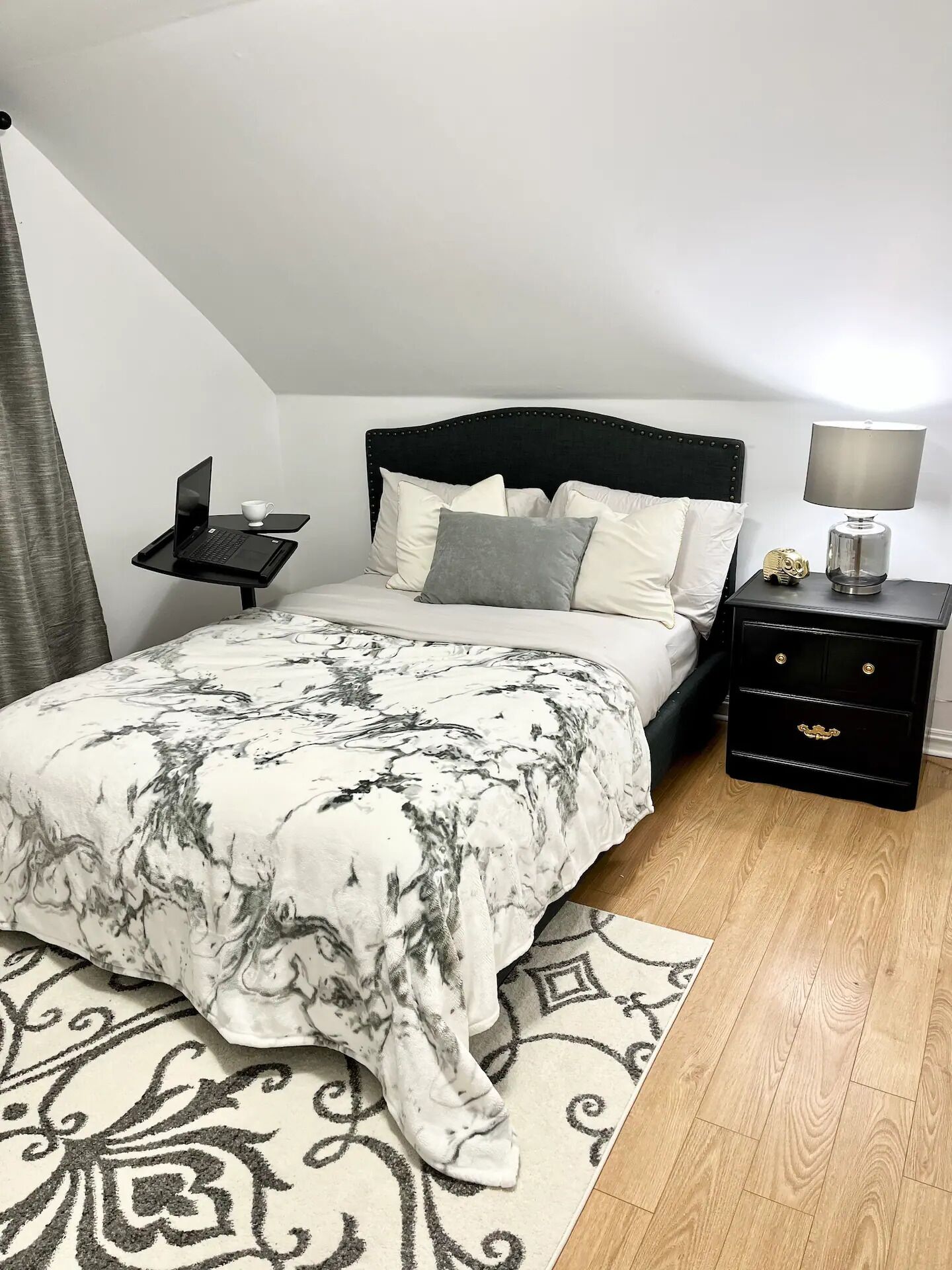Une chambre à coucher avec un lit, des tables de chevet, une lampe et un ordinateur portable posé sur un plateau.
