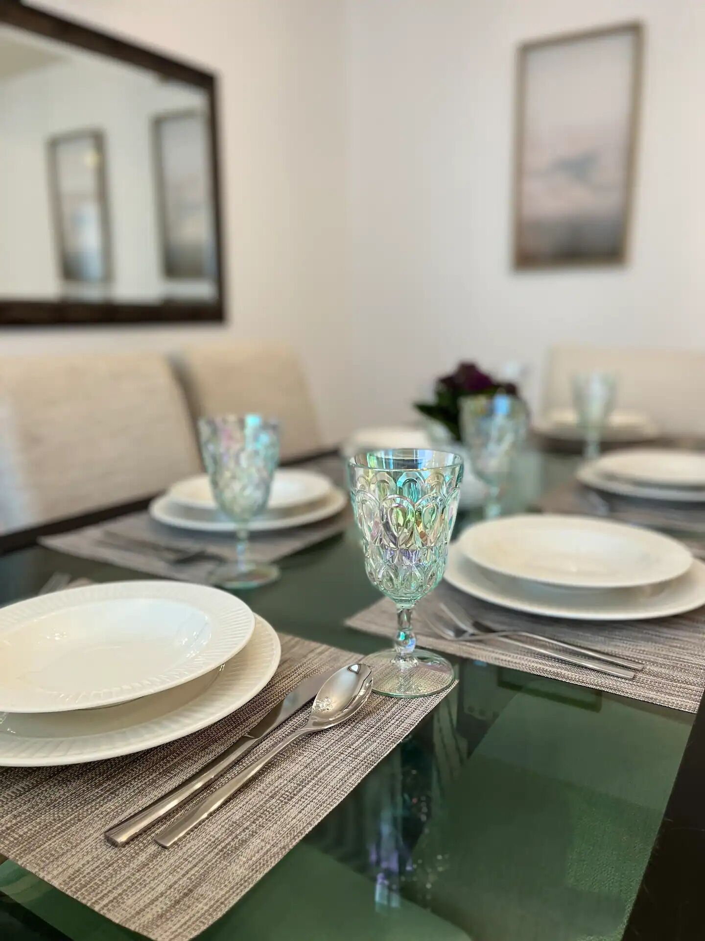 A dining table set with plates, cutlery, and glassware, with a sofa and a painting in the background.
