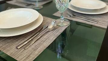 A dining table set with plates, cutlery, and glassware, with a sofa and a painting in the background.