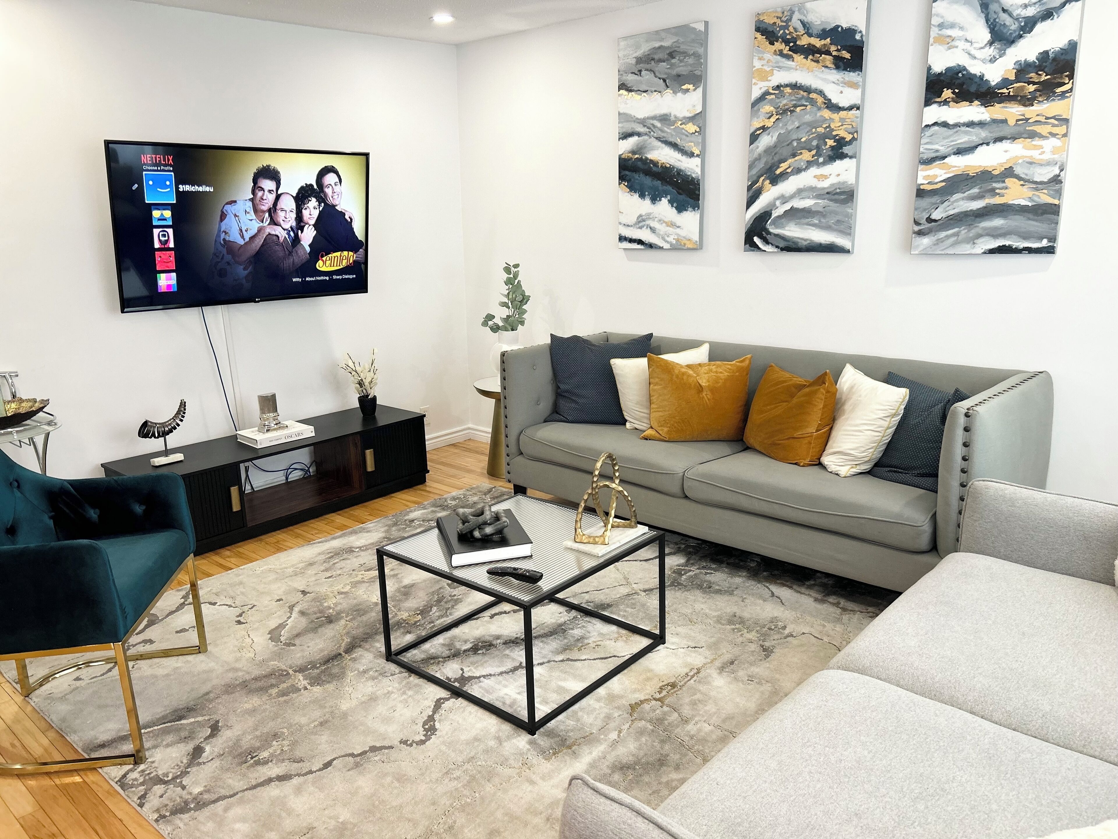 Un salon moderne avec un téléviseur à écran plat, un canapé gris agrémenté de plusieurs coussins, une table basse et un fauteuil bleu.