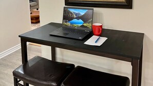 Une petite cuisine équipée d’un réfrigérateur, d’un four à micro-ondes et de placards. Un ordinateur portable est posé sur une table, à côté d’une tasse rouge. Deux chaises se trouvent devant la table.