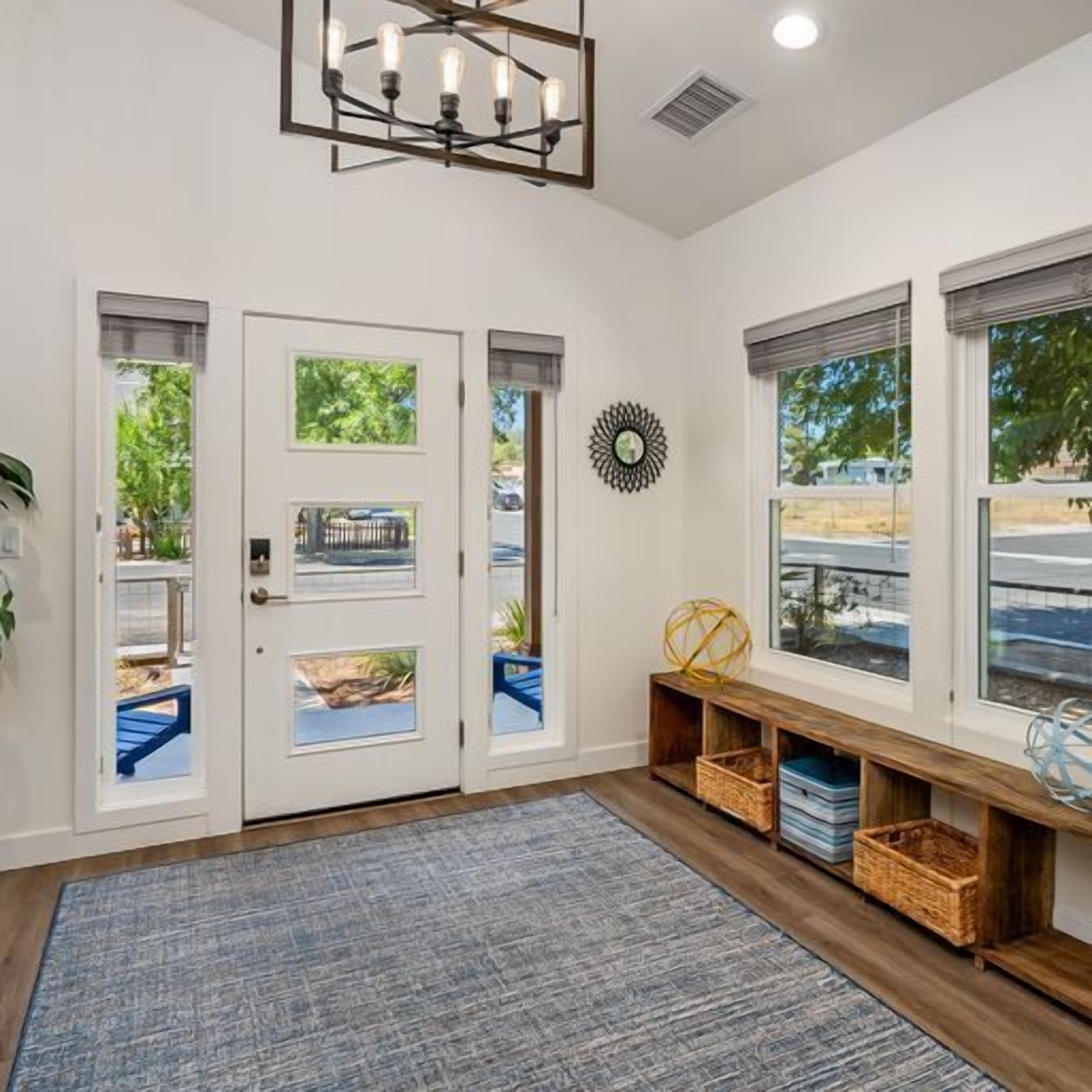A modern entryway with a blue textured rug, a wooden bench with baskets, and a decorative mirror.