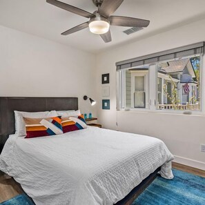 Ein Schlafzimmer mit Bett, Deckenventilator, Fenster und Nachttisch mit Lampe.