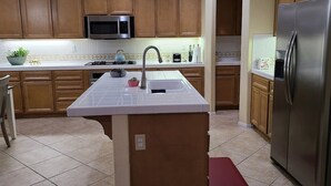 A kitchen with wooden cabinets, a stainless steel refrigerator, a microwave, and a sink with a tiled countertop. - This house is a 5 bedroom(s), 3 bathrooms, located in Eastvale , CA. (Eastvale)