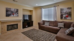 A living room with a fireplace, a sofa, and two paintings on the walls. - This house is a 5 bedroom(s), 3 bathrooms, located in Eastvale , CA. (Eastvale)