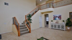 A spacious foyer with a wooden staircase, a white console table with plants, and a painting on the wall. - This house is a 5 bedroom(s), 3 bathrooms, located in Eastvale , CA. (Eastvale)