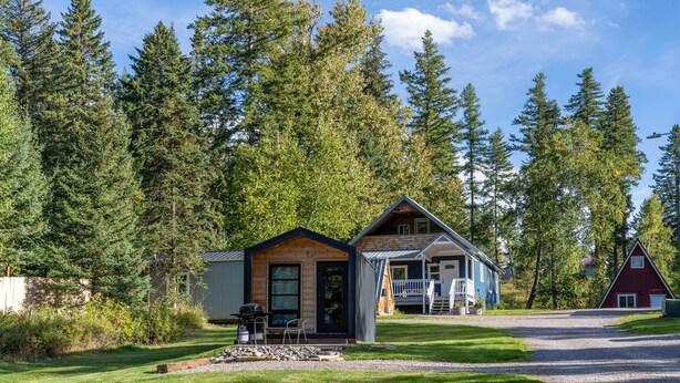 Een chalet met een veranda en een apart gebouw, omgeven door dicht bos.