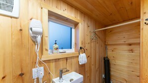 Een badkamer met houten lambrisering, een raam, een haardroger, een wastafel en een handdoekhouder.